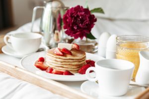 Breakfast in bed with white linen. Pancakes, boiled eggs, coffee